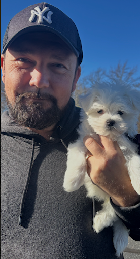 A man holding a white puppy outdoors